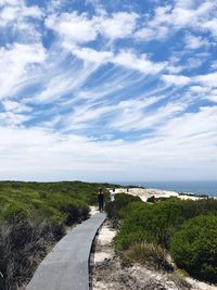 Rear view of woman walking on boardwalk at beach against sky