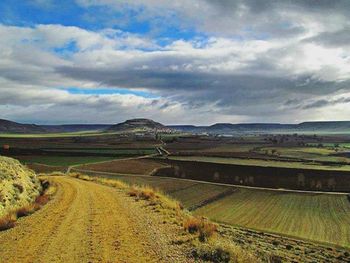 Road passing through field against cloudy sky