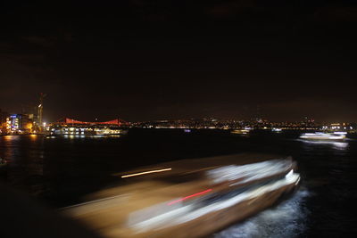 Illuminated city by sea against sky at night