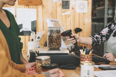 Saleswoman scanning mason jar on weight scale by customers at checkout counter