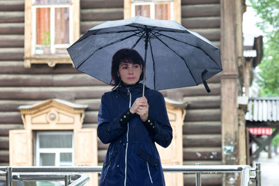An adult woman with umbrella walks down street peering into people's faces on a cloudy rainy day.