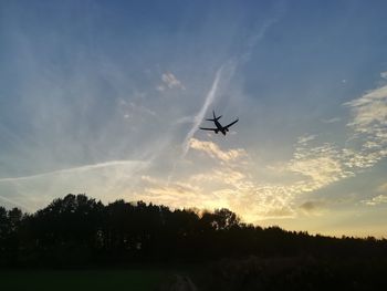 Low angle view of silhouette airplane flying against sky during sunset