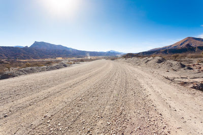 Dirt road amidst desert against sky