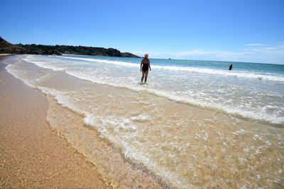 Rear view of woman standing on shore at beach against sky