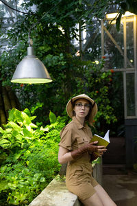 Portrait of woman sitting by plants against trees