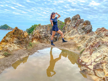 Full length of young woman standing on rock against sky