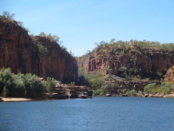 Scenic view of cliff by trees against clear sky