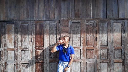 Young man drinking cola while standing against wooden doors