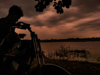 Silhouette man riding bicycle on shore against sky during sunset