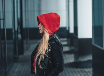 Young woman wearing hood while standing by building