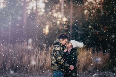 Side view of romantic couple standing at forest during snowfall