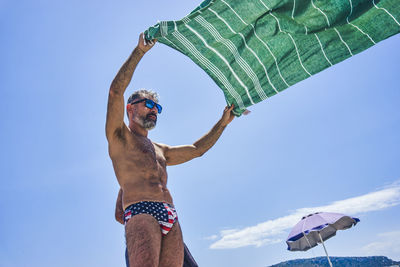 Man in costume shaking a beach towel on a sunny beach in sardinia