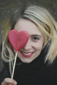 Close-up portrait of smiling woman with heart shape lollipop