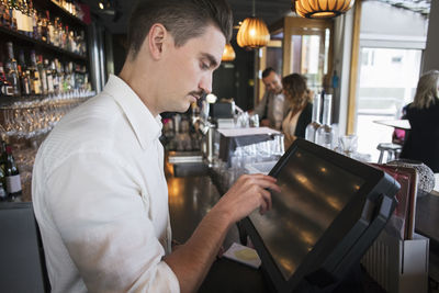 Side view of male owner using cash register at checkout in restaurant