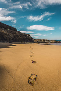 Footprints on sand at beach against sky