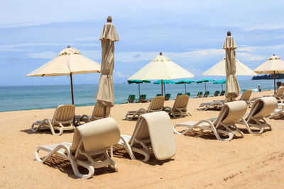 Lounge chairs and parasols on beach against sky