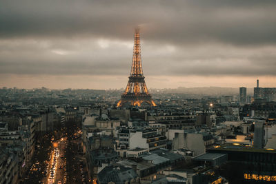 Illuminated buildings in city against cloudy sky