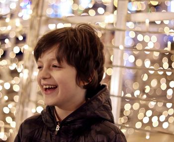 Close-up of cheerful boy looking away against illuminated lights