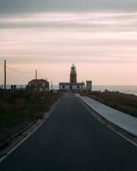 Road leading towards lighthouse against sky during sunset