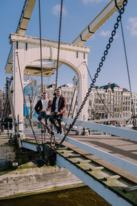 Full length of men sitting on bridge against sky