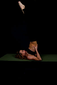 Athlete doing shoulder stand on exercise mat against black background