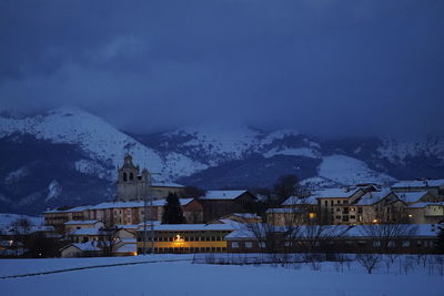 Snow covered houses by building against sky at dusk