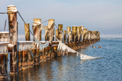 Wooden posts in sea against sky