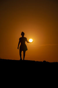 Silhouette man standing on field against sky during sunset