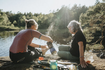 Two senior women preparing hot meal at campsite at lakeshore