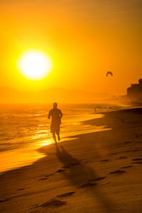 Silhouette man running on beach against orange sky during sunset