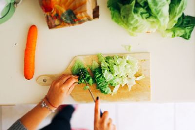 Cropped hands of woman cutting vegetables on table in kitchen