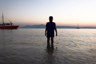 Rear view of man standing on sea against sky during sunset