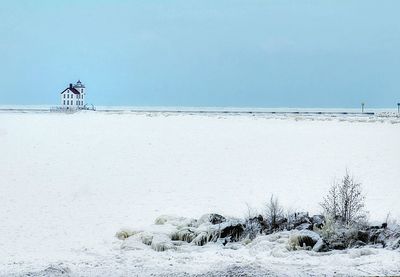 Lighthouse by lake erie against clear blue sky during winter