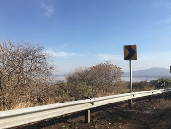 Road sign by trees on field against sky