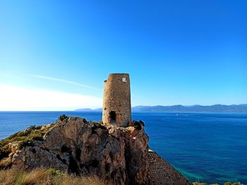 Spanish age tower by sea against blue sky in cagliari