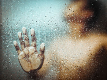 Close-up of hand touching wet glass window