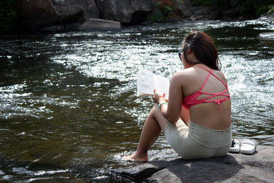 Full length of a woman reading a book beside a river.