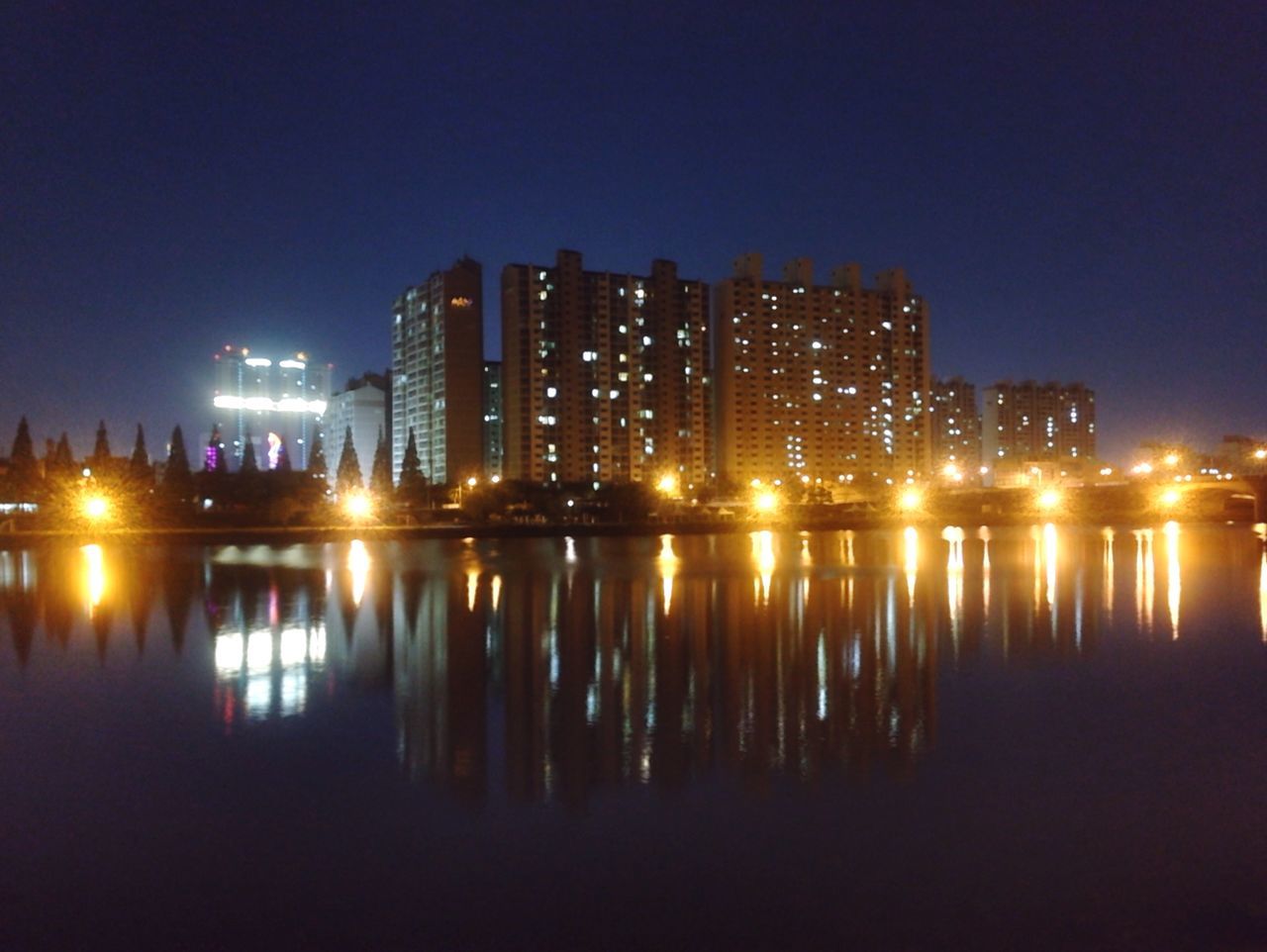 illuminated, night, reflection, water, building exterior, architecture, waterfront, city, built structure, river, clear sky, cityscape, skyscraper, light, lighting equipment, sky, copy space, no people, mid distance, outdoors