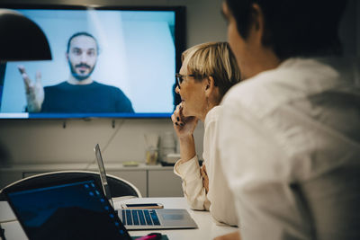 Colleagues listening to businessman during video conference in board room at office