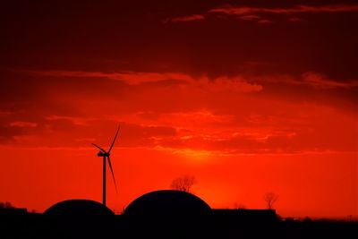 Silhouette of wind turbine against cloudy sky during sunset in red colour