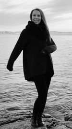 Smiling woman standing on rock by sea