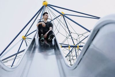 Low angle view of man sitting on slide against sky