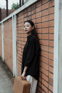 Young woman standing against brick wall