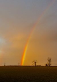 Scenic view of rainbow over field during sunset
