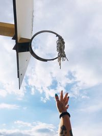 Cropped hand of woman gesturing by basketball hoop against sky