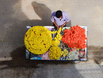 High angle view of man preparing flower garland on roadside in city