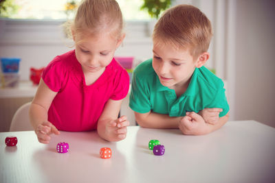 Cute smiling sibling playing with dice on table at home