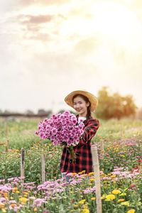 Portrait of smiling young woman standing by flowering plants on field