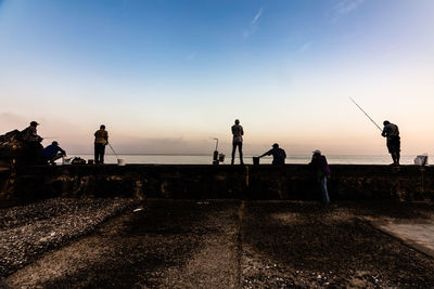 Silhouette people fishing at sea against sky during sunset
