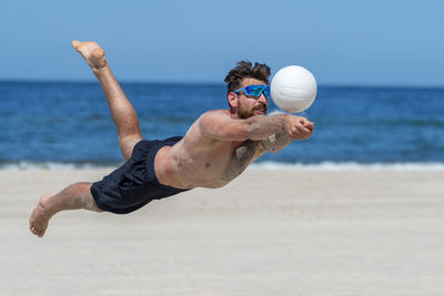 Shirtless man playing volleyball at beach